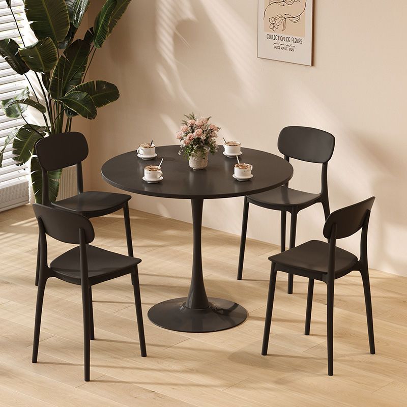 Round black tulip table with four black chairs and flowers in a sunlit room