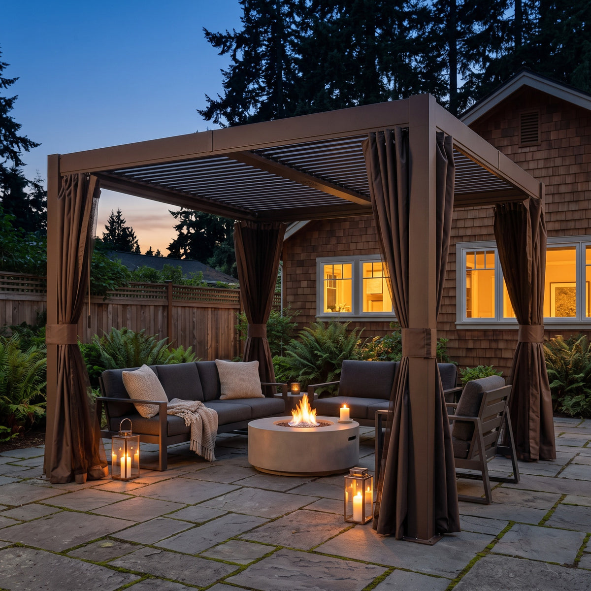 Brown aluminum louvered pergola with tied back curtains over a sofa and fire pit on a stone patio at dusk