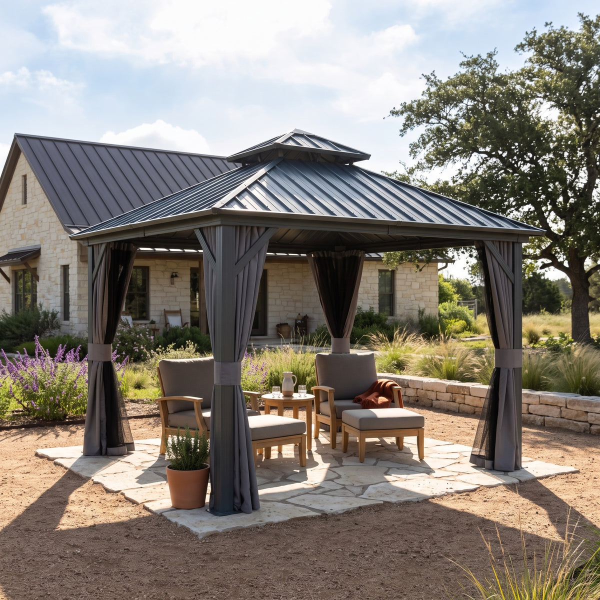 Gray aluminum 10x10 hardtop gazebo with tied back curtains over wood lounge chairs on a stone pad in daylight