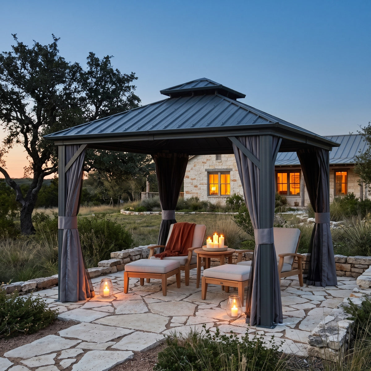 Gray aluminum 10x10 double roof hardtop gazebo with tied back curtains over lounge chairs on a stone patio at dusk