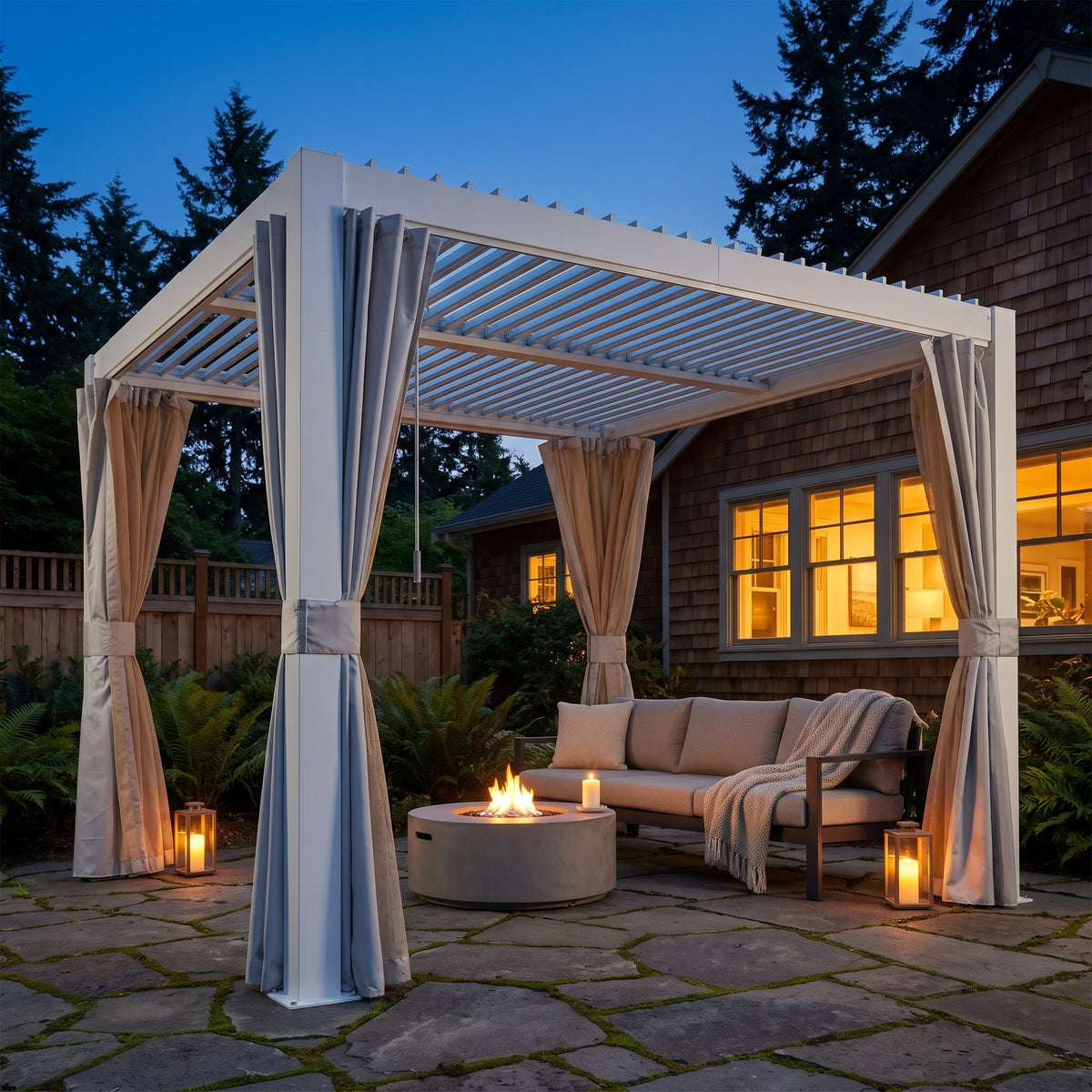 White aluminum 10x10 louvered pergola with tied curtains over a sofa and fire pit on a stone patio at dusk