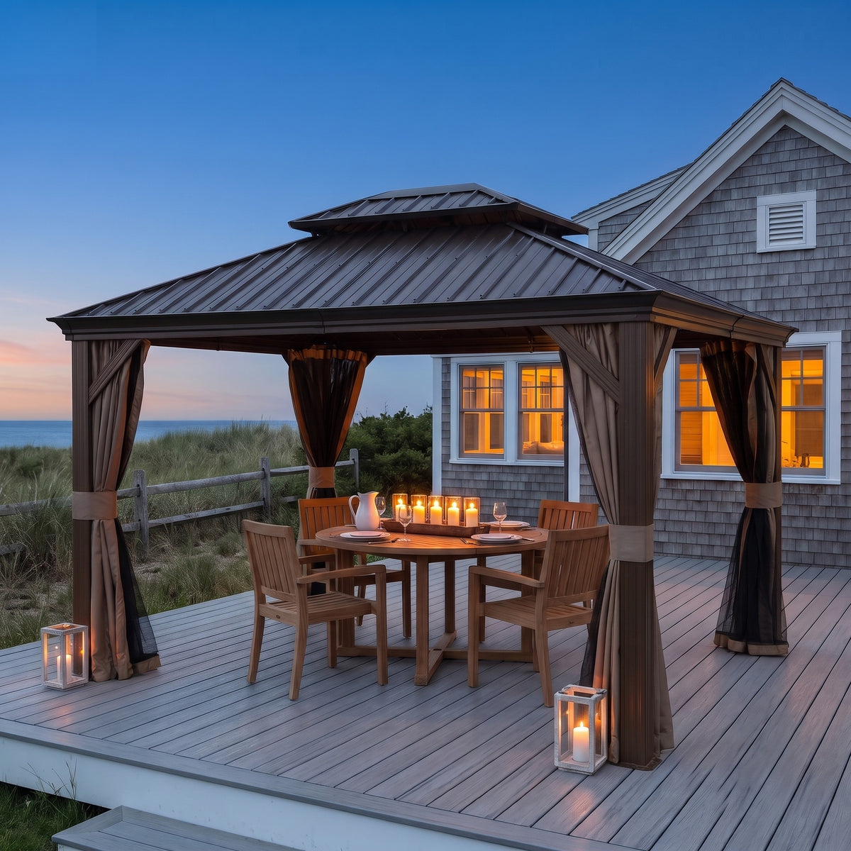 Brown 10x12 hardtop gazebo with tan curtains over a candlelit dining table on a seaside deck at dusk