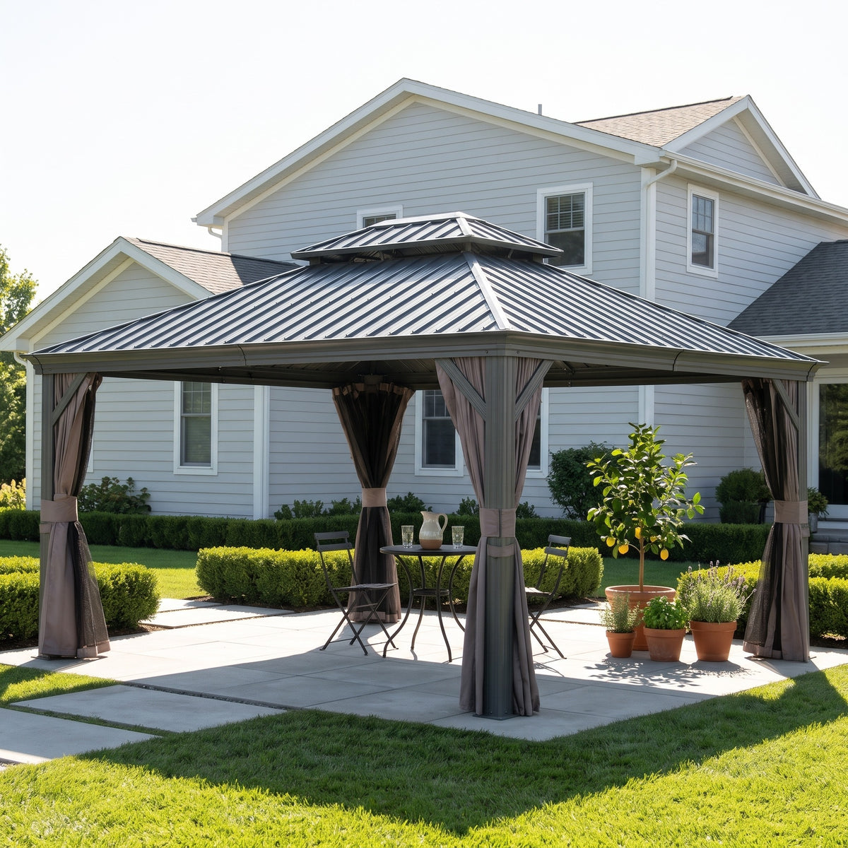 Gray double roof hardtop gazebo with tied back curtains over a bistro table on a concrete patio by a house