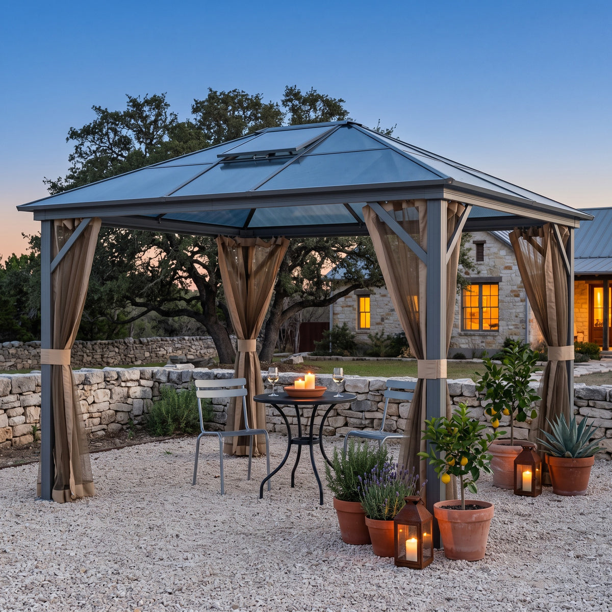 Gray aluminum hardtop gazebo with tan mesh netting over a bistro table on a gravel patio at dusk with candle lanterns