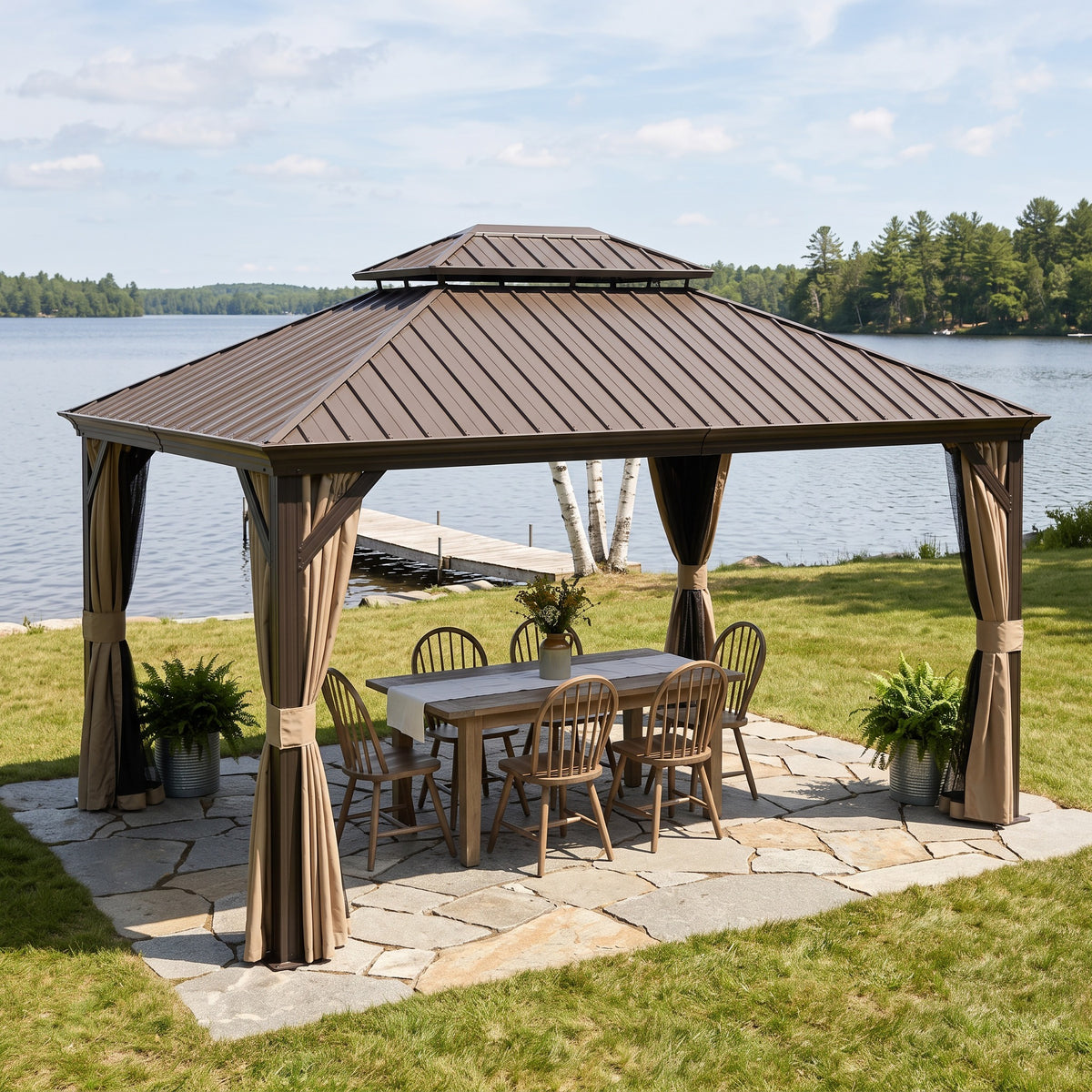 Brown metal double roof hardtop gazebo with tan curtains over a dining table on a stone patio by a lake