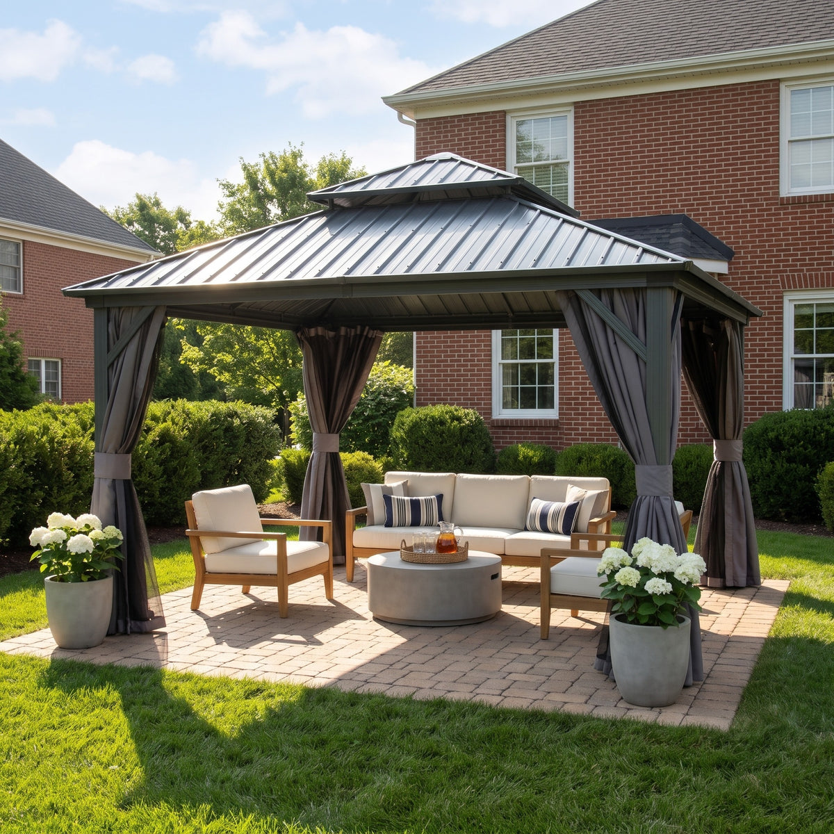 Gray aluminum 12x12 double roof hardtop gazebo with tied back curtains over a patio sofa set on a sunny lawn
