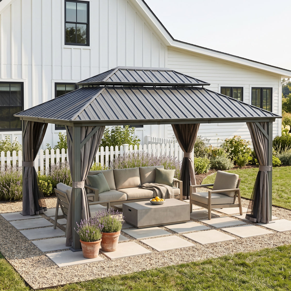 Gray aluminum 12x14 double roof hardtop gazebo with tied back curtains over a sofa set on a gravel and paver patio