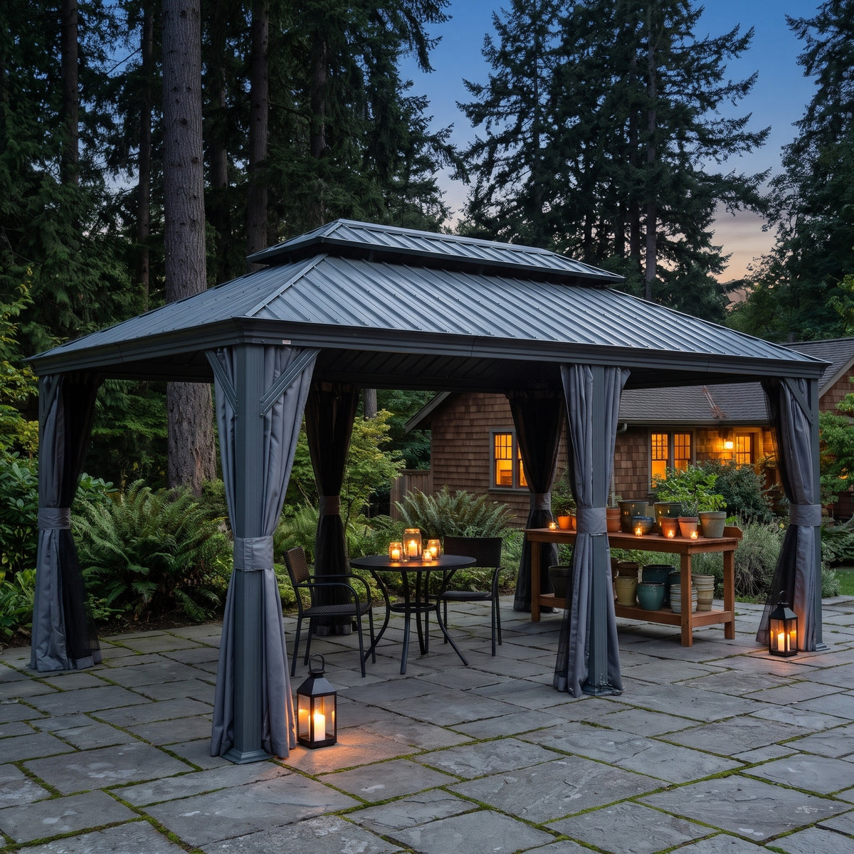 Gray 12x20 hardtop gazebo with tied back curtains over a bistro table on a stone patio at dusk with lanterns