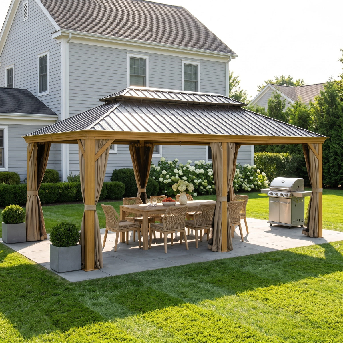 Yellow brown aluminum 12x20 hardtop gazebo with tan curtains over a dining table on a stone patio in a sunny yard