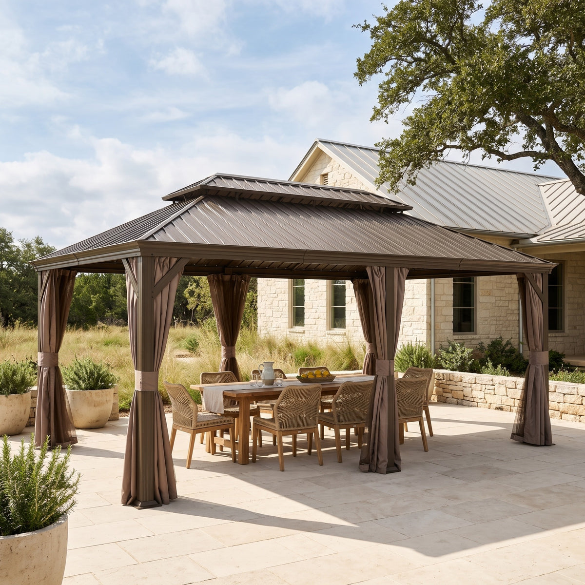 Brown 14x20 hardtop gazebo with tied back curtains over a wood dining table on a stone patio in daylight