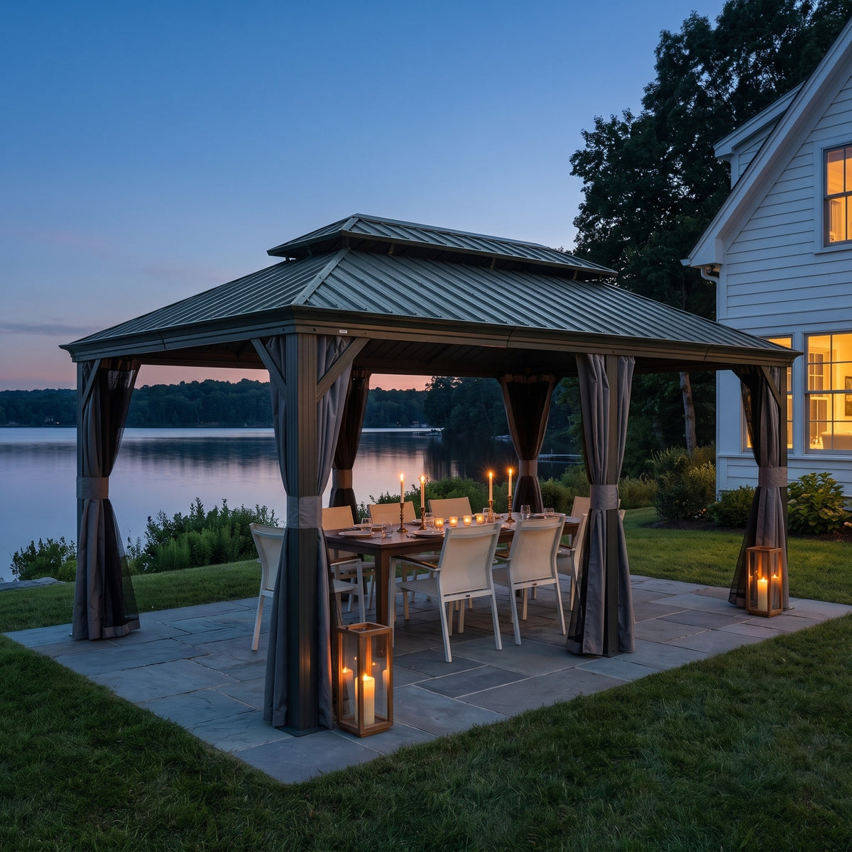 Gray double roof hardtop gazebo with curtains over a candlelit dining table on a stone patio by a lake at dusk