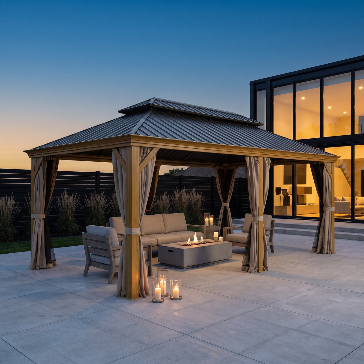 Wood grain aluminum 14x20 hardtop gazebo with tan curtains over a lounge set on a concrete patio at dusk