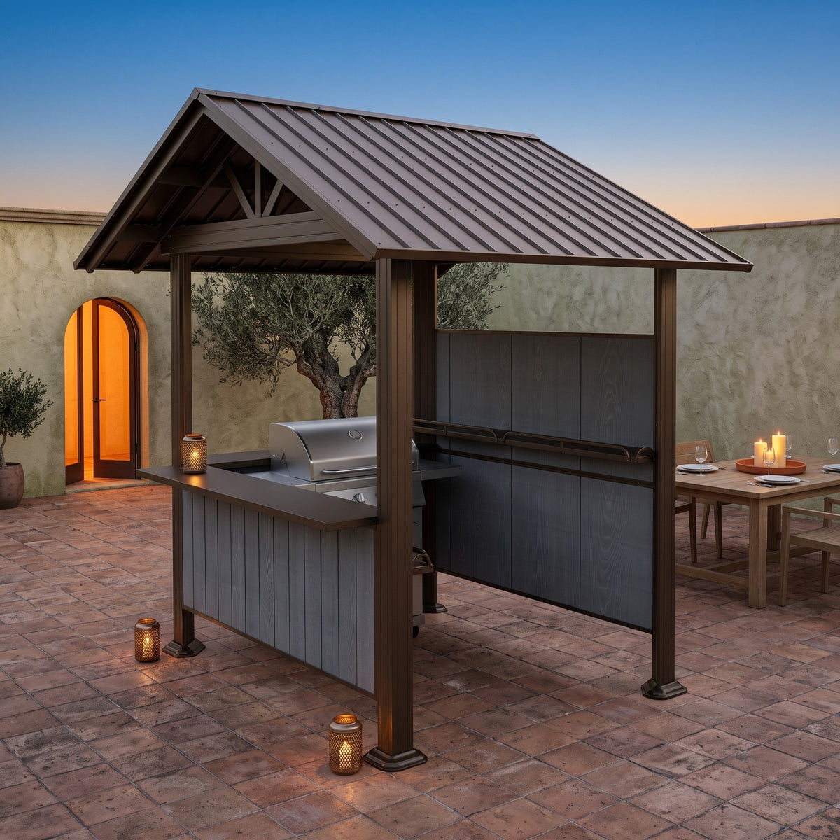 Brown steel gable roof grill gazebo with gray side panels and counter on a terracotta courtyard at dusk with lanterns