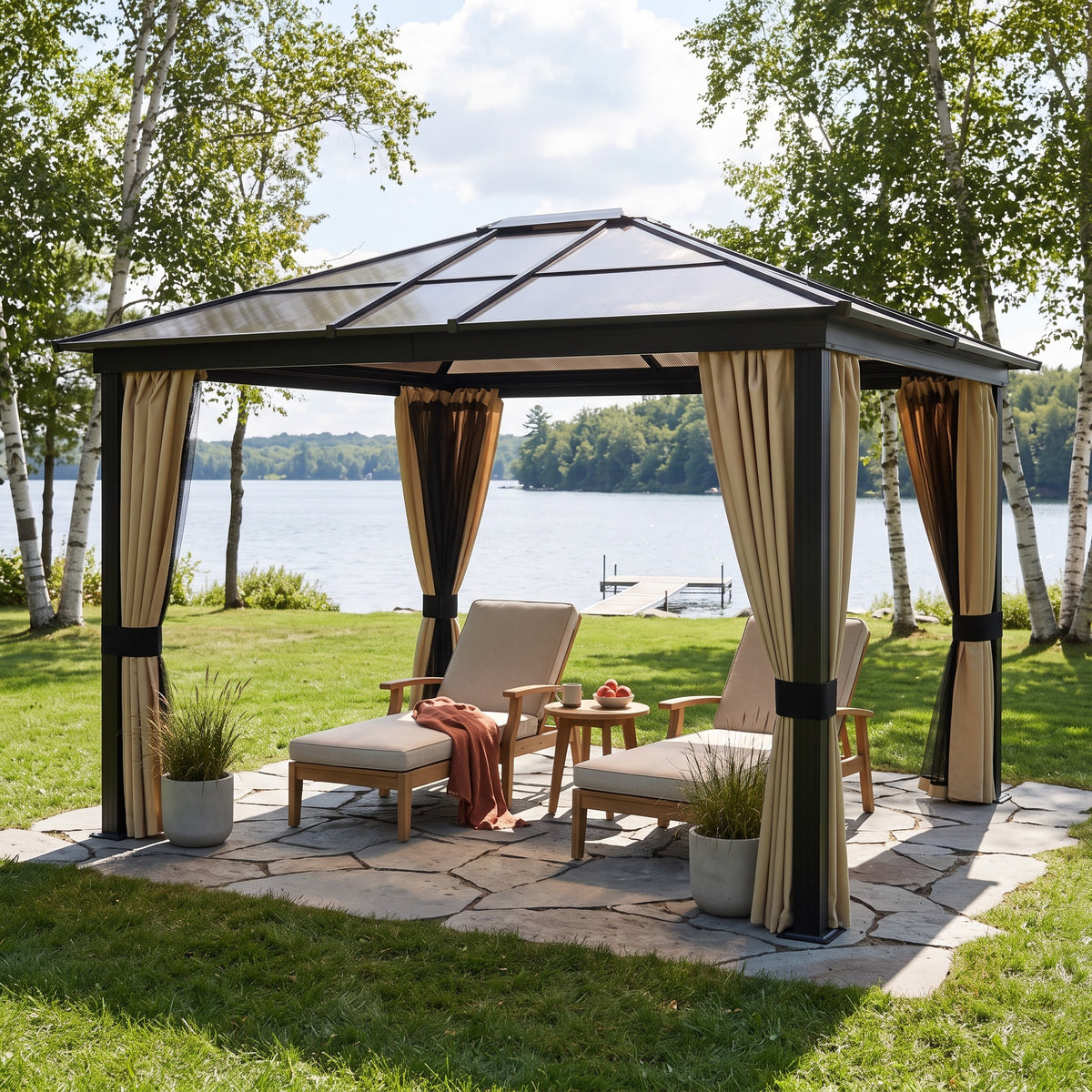 Gray aluminum hardtop gazebo with beige curtains over two chaise lounges on a stone patio by a lake