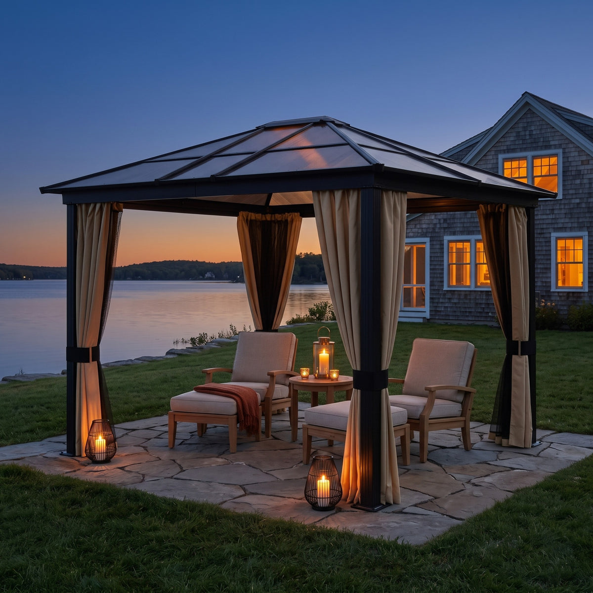 Aluminum hardtop gazebo with beige curtains over lounge chairs on a stone patio by a lake at dusk