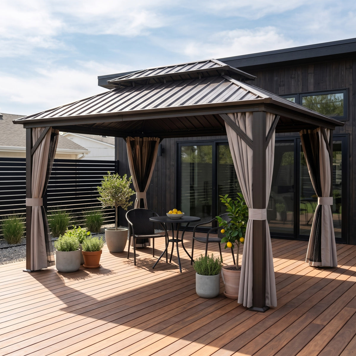 Brown double roof hardtop gazebo with tied back curtains over a bistro table on a wood deck in daylight