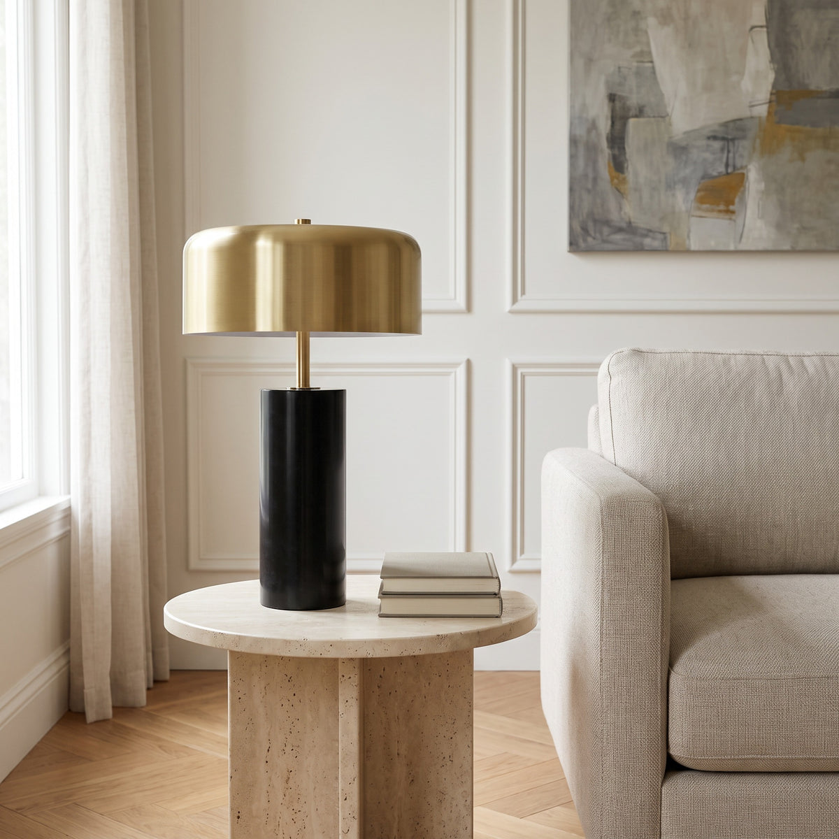 Black marble table lamp with brass finish drum shade on a round stone side table beside a beige sofa