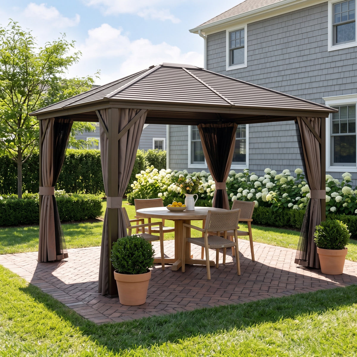 Bronze aluminum hardtop gazebo with tied-back curtains over a round wood dining table on a brick patio