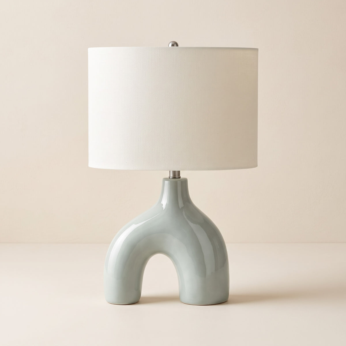 Sage green ceramic arch table lamp with ivory linen drum shade on a warm ivory backdrop