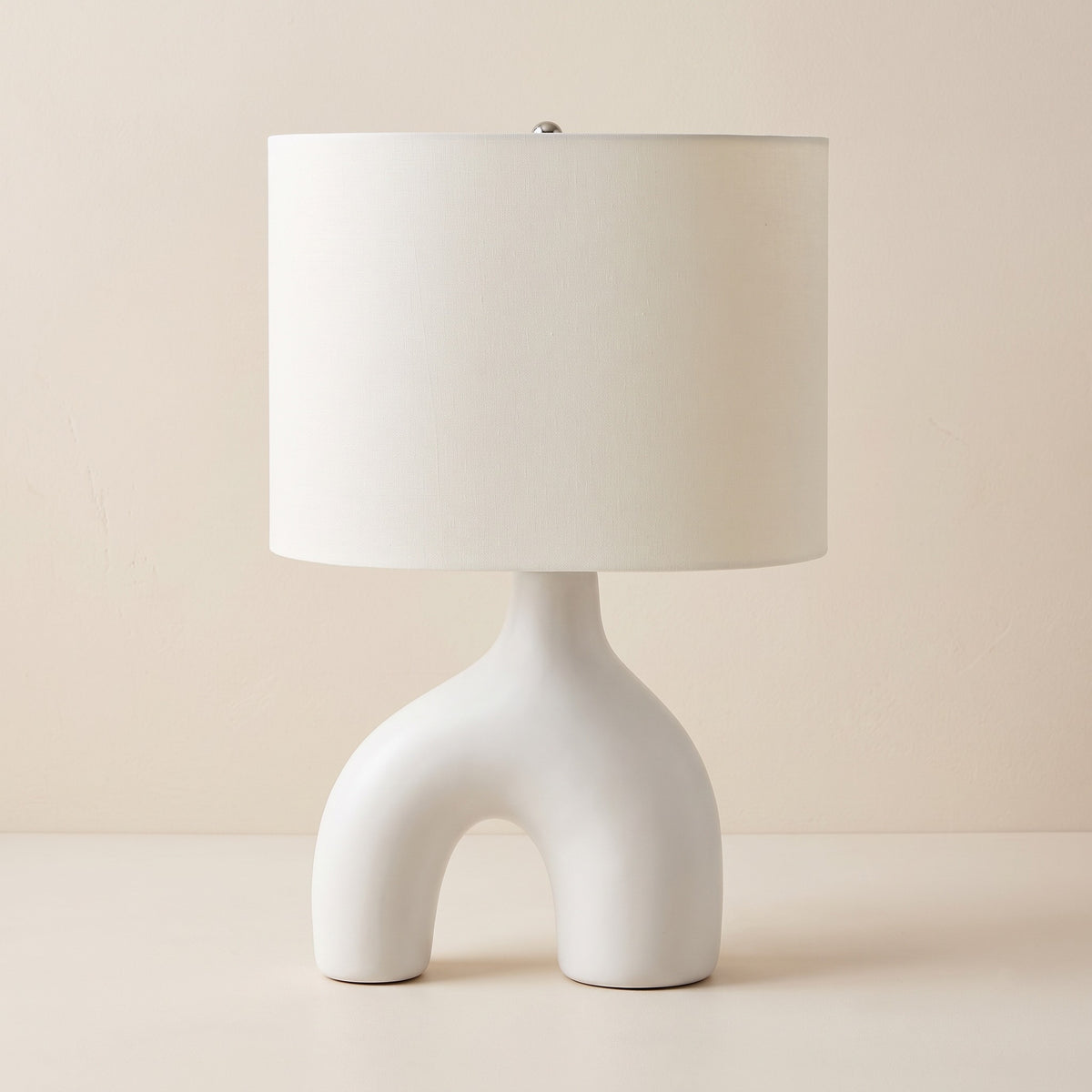 White ceramic arch table lamp with white fabric drum shade on an ivory plaster backdrop