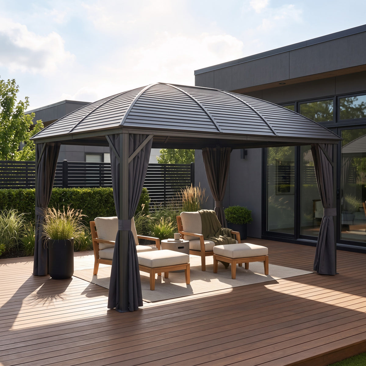 Dark gray aluminum hardtop gazebo with tied back curtains over teak lounge chairs on a wood deck in daylight
