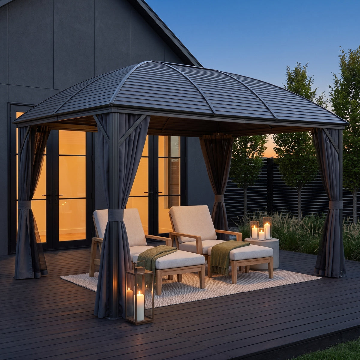 Dark gray aluminum hardtop gazebo with tied back curtains over lounge chairs on a deck at dusk, lit by candle lanterns