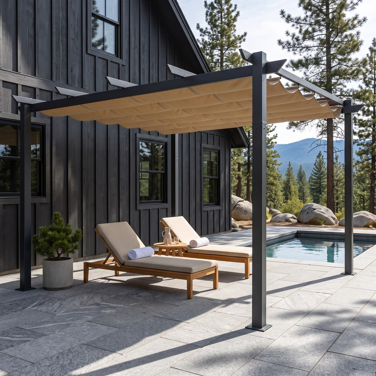 Dark gray aluminum pergola with tan retractable canopy over two loungers beside a pool on a stone patio in daylight