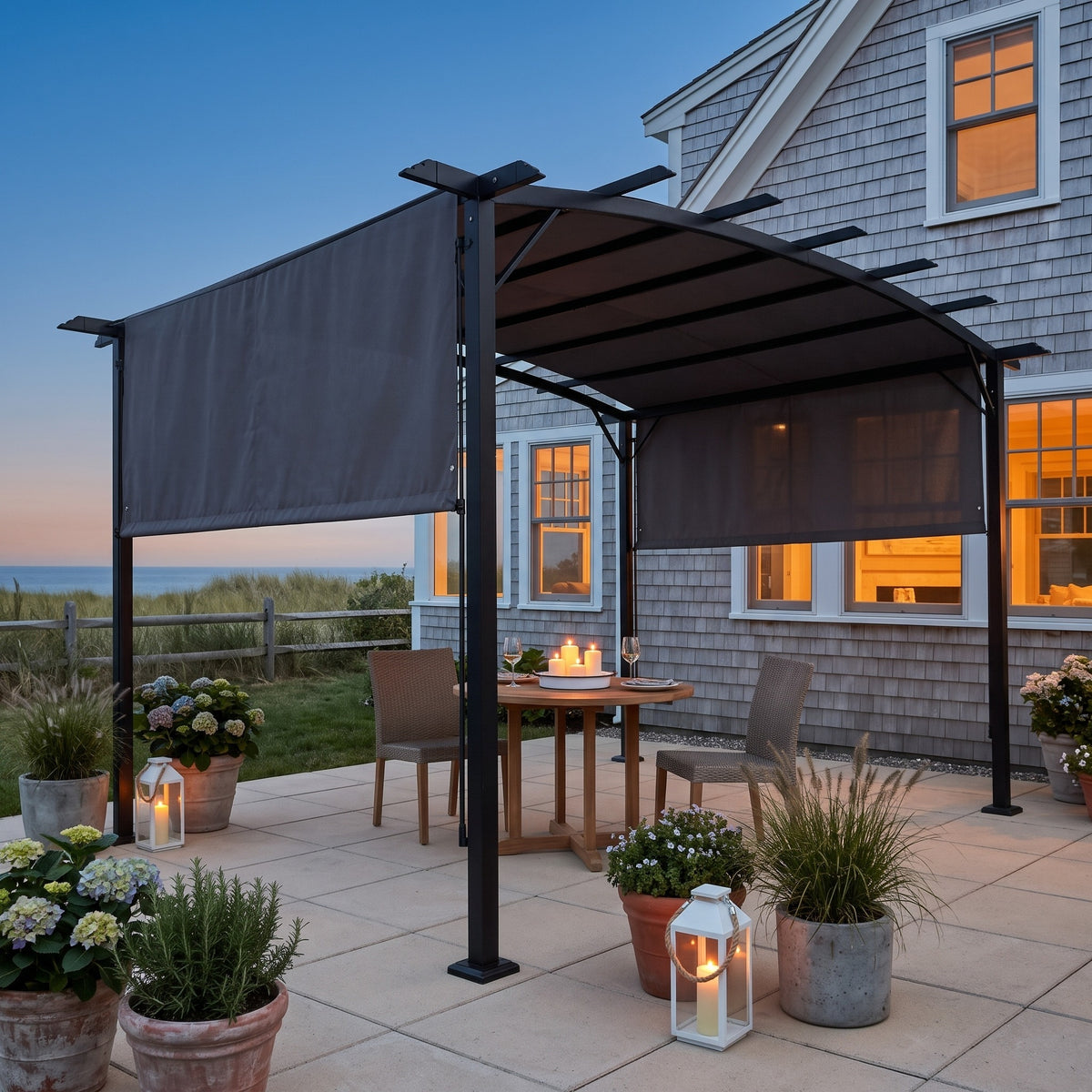 Gray metal pergola with arched canopy and side shades over a round table on a seaside patio at dusk