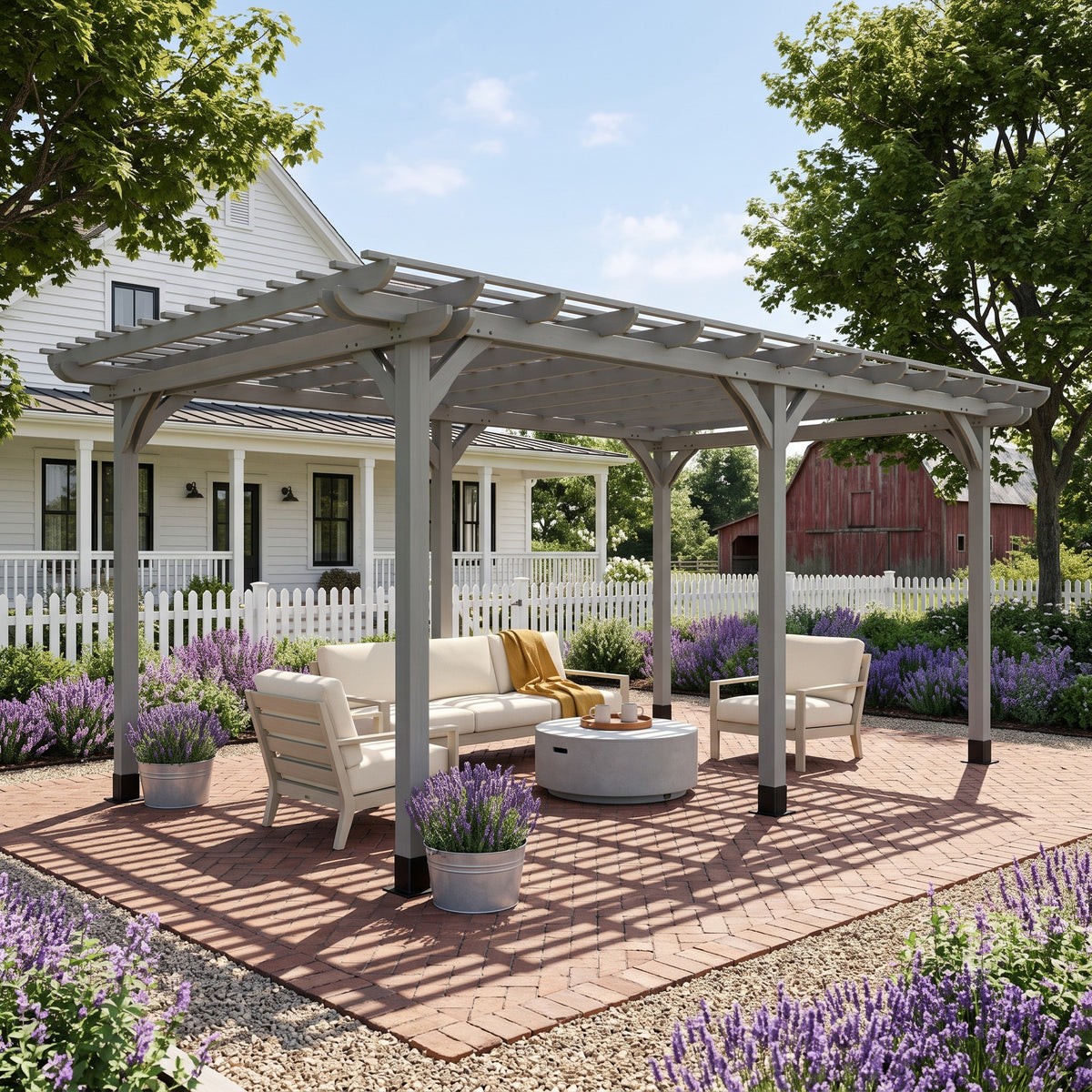 Gray wood pergola over cream outdoor sofa and chairs on a brick patio, lavender beds and a farmhouse behind