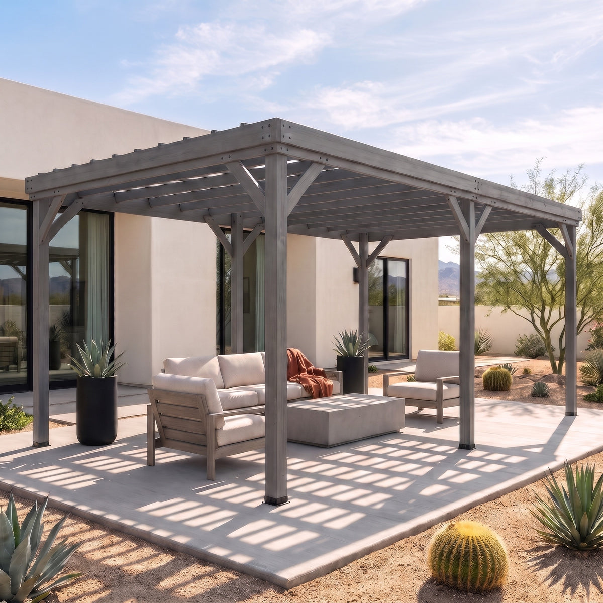 Gray wood 12x20 pergola shading an outdoor sofa and chairs on a concrete patio beside a desert garden