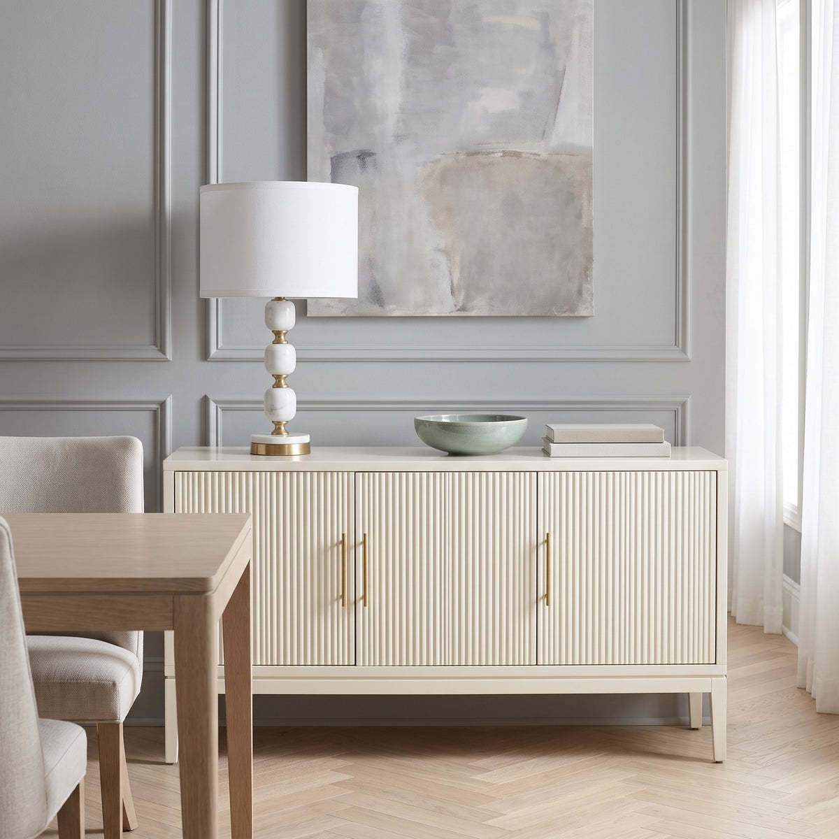 White marble table lamp with brass accents and white drum shade on an ivory fluted sideboard in a dining room