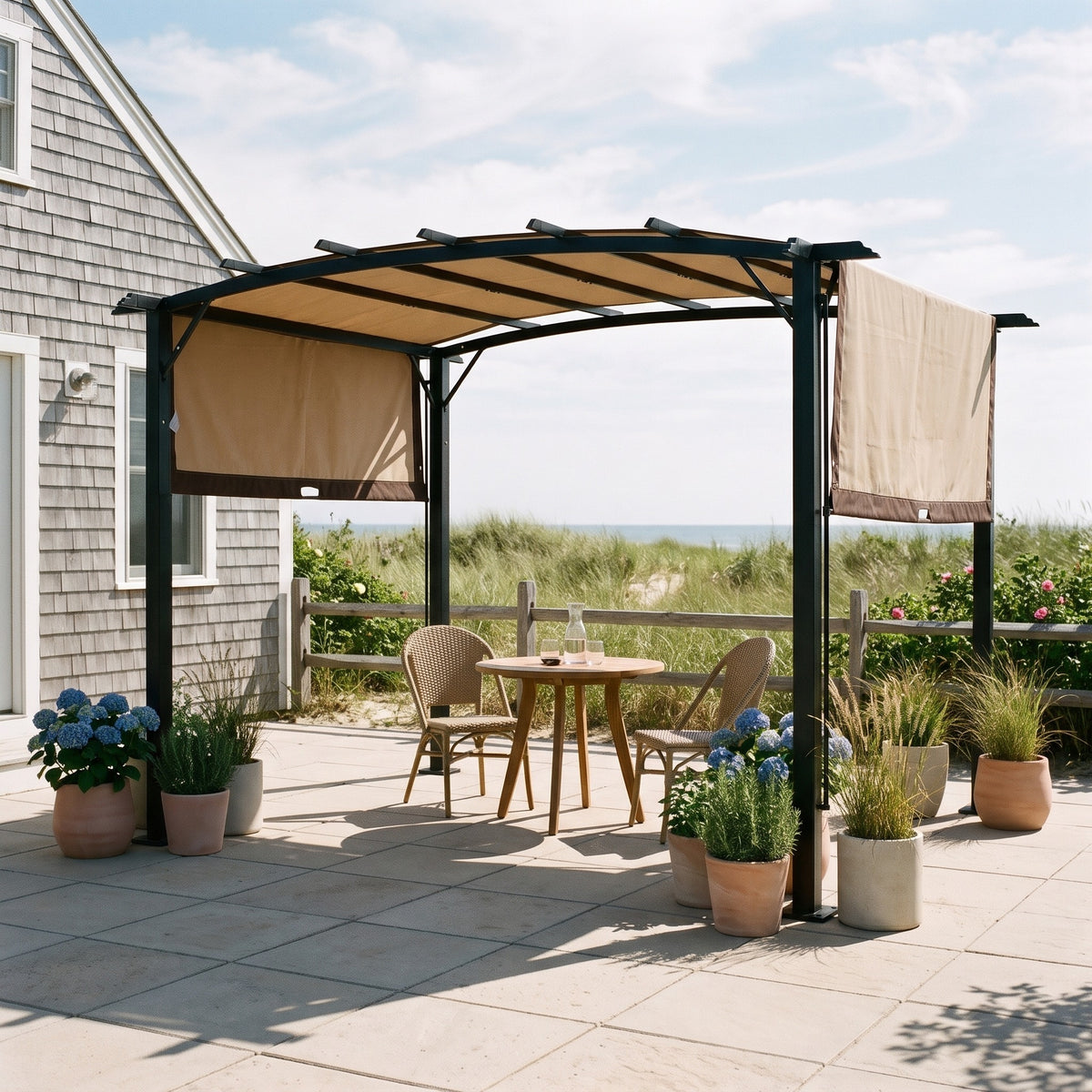 Black steel pergola with beige retractable canopy over a bistro table on a coastal stone patio