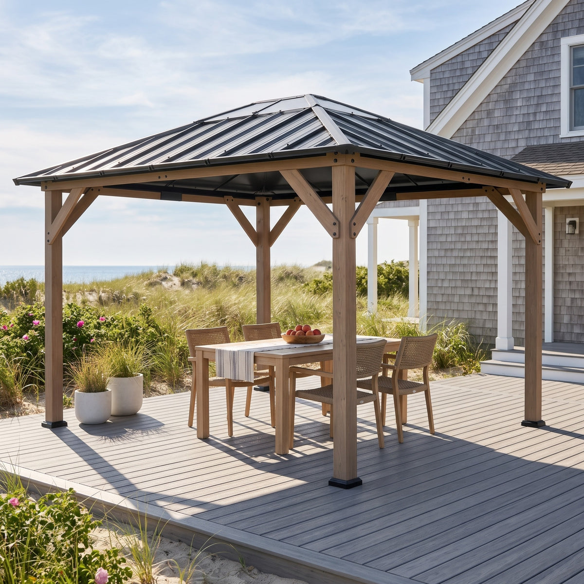 Walnut wood hardtop gazebo with gray steel roof over a dining table on a gray deck by beach dunes