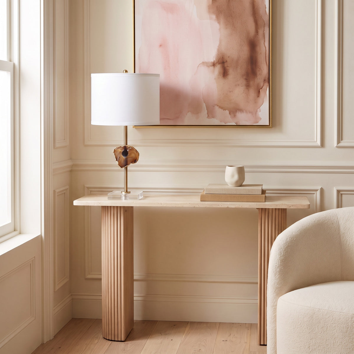 Table lamp with agate slice on a brass stem, white drum shade and clear acrylic base on a travertine console
