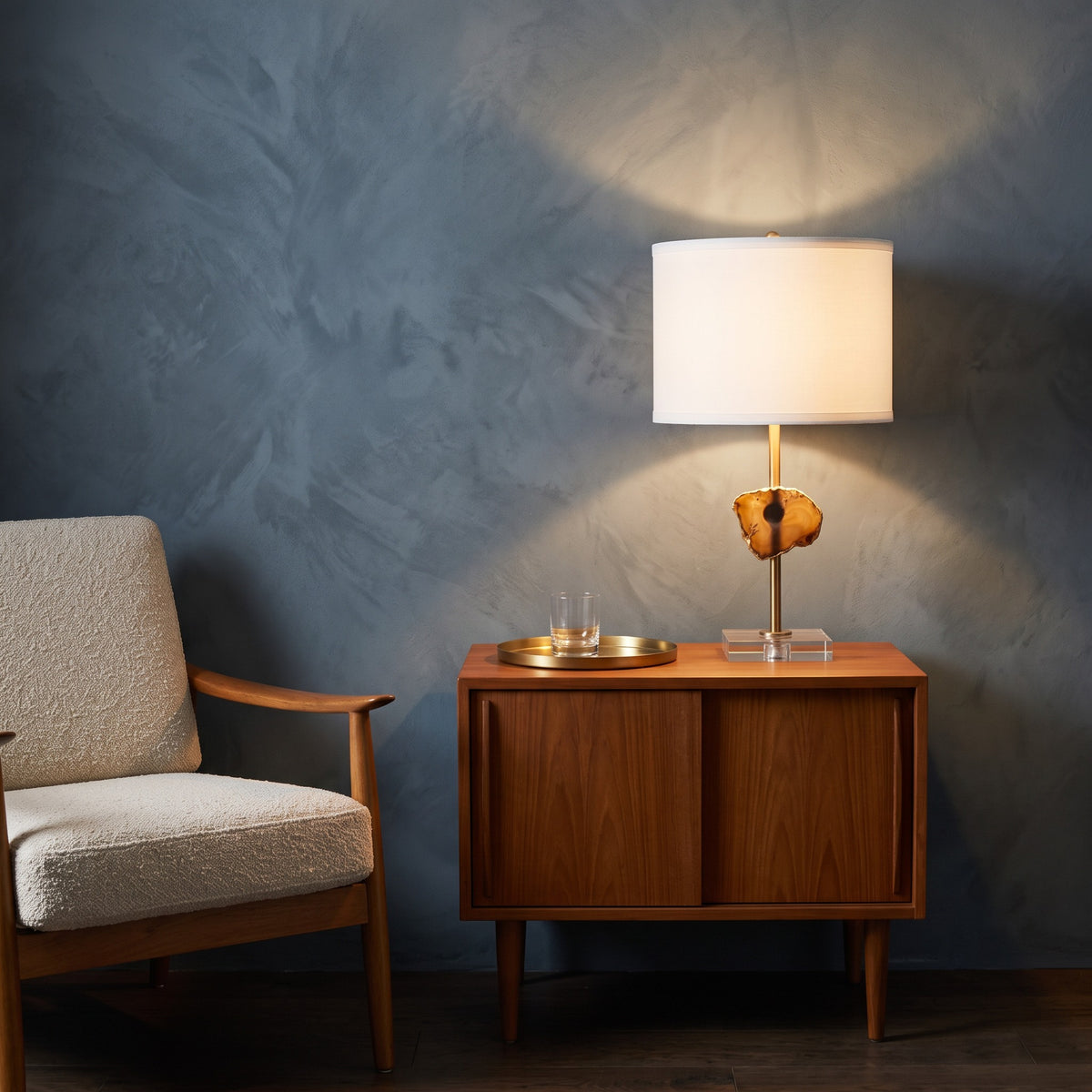 Gold and white table lamp with agate slice, acrylic base and white drum shade, lit on a walnut cabinet by an armchair