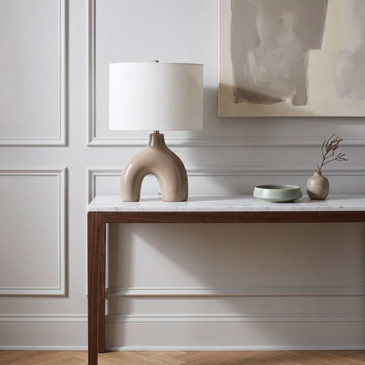 Light brown glossy ceramic arch table lamp with white fabric drum shade on a marble top walnut console
