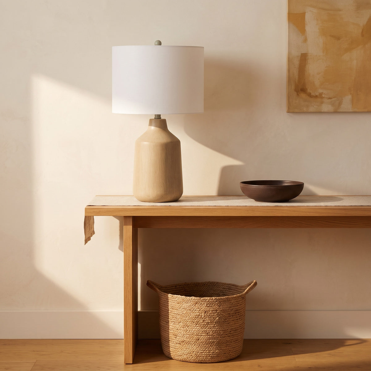 Beige concrete table lamp with white drum shade on an oak console table beside a dark bowl