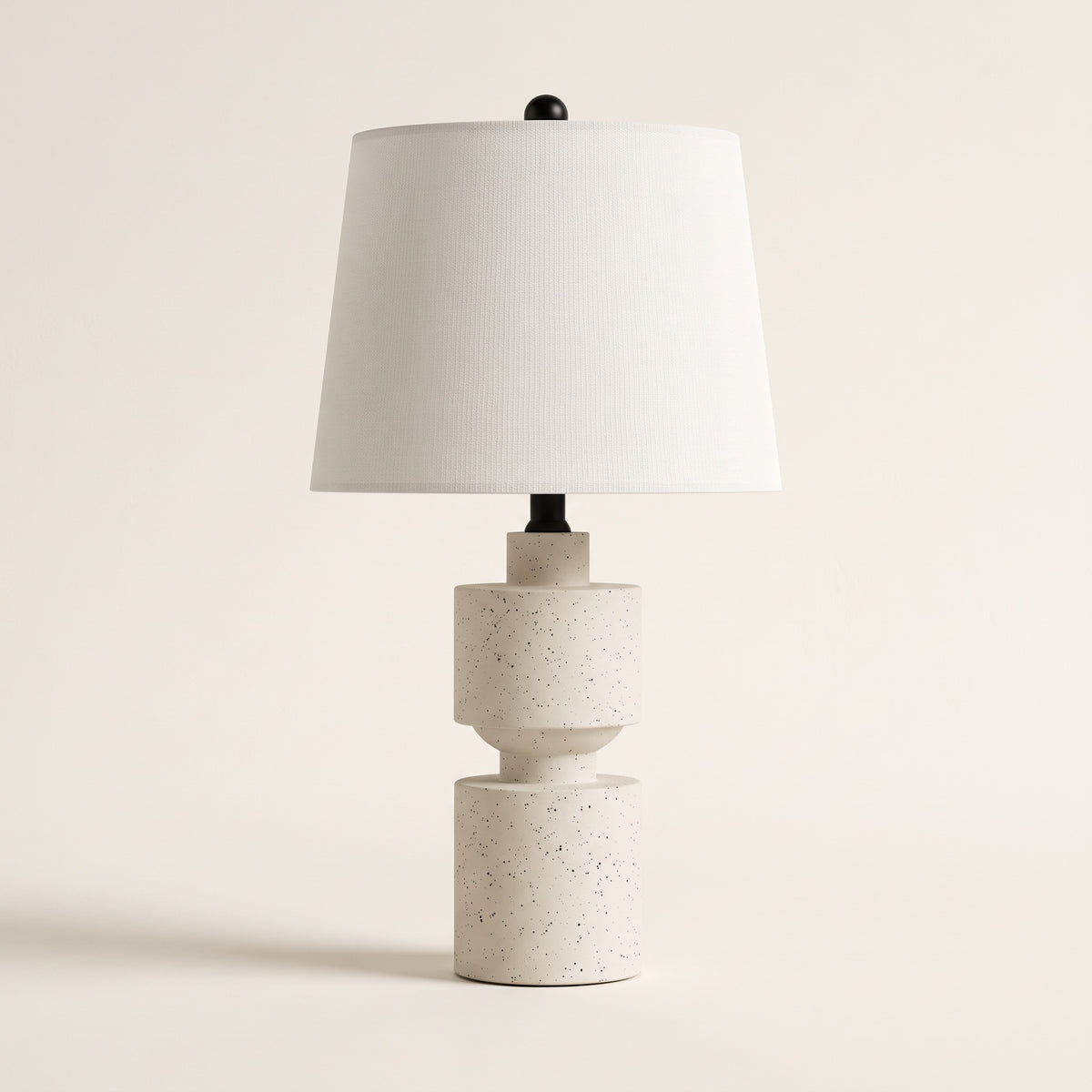 Speckled white resin table lamp with white linen-look tapered drum shade on an ivory backdrop