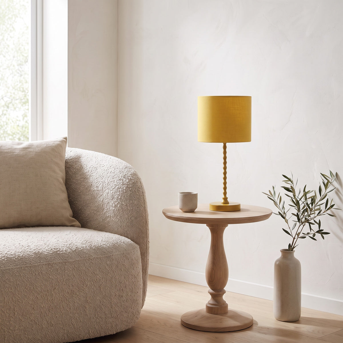 Yellow table lamp with beaded metal stem and linen-look drum shade on an oak pedestal side table beside a sofa