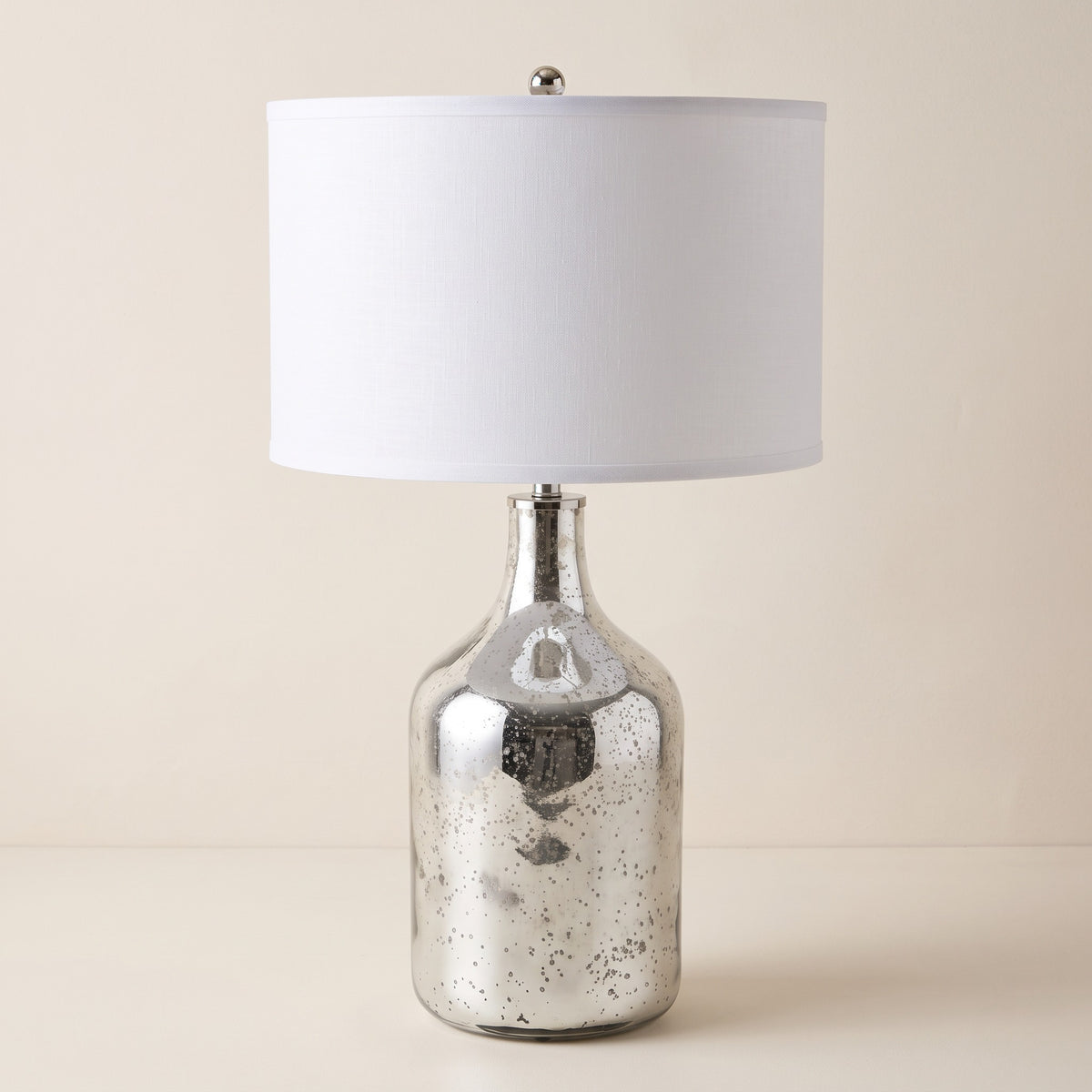 Silver speckled glass table lamp with white fabric drum shade on an ivory backdrop