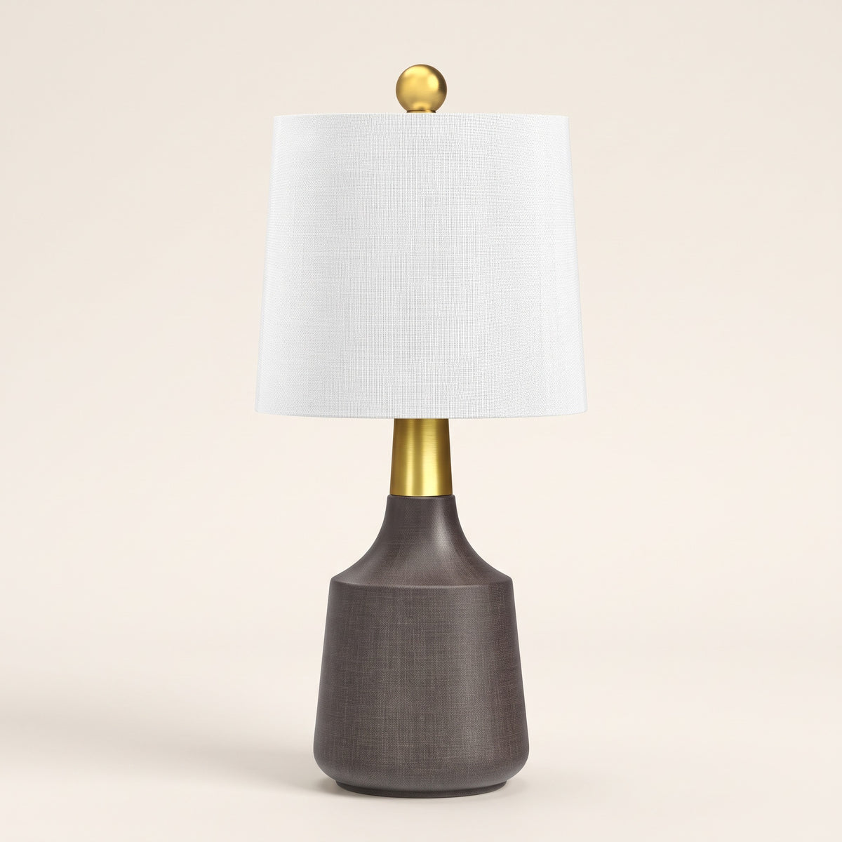 Gray ceramic table lamp with white linen drum shade and brass neck on an ivory backdrop