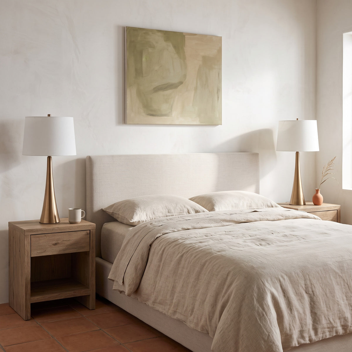 Two bronze table lamps with white linen shades on oak nightstands beside a bed with linen bedding