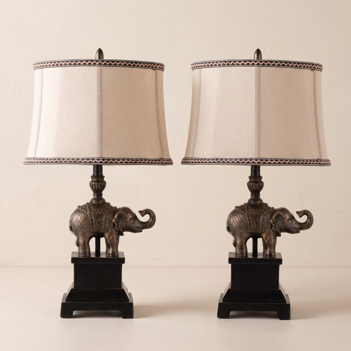 Pair of bronze finish elephant table lamps with natural linen shades on a warm ivory plaster backdrop