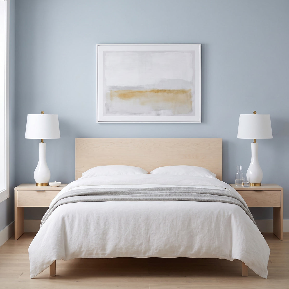 Pair of white ceramic table lamps with brass feet and white drum shades on maple nightstands beside a bed