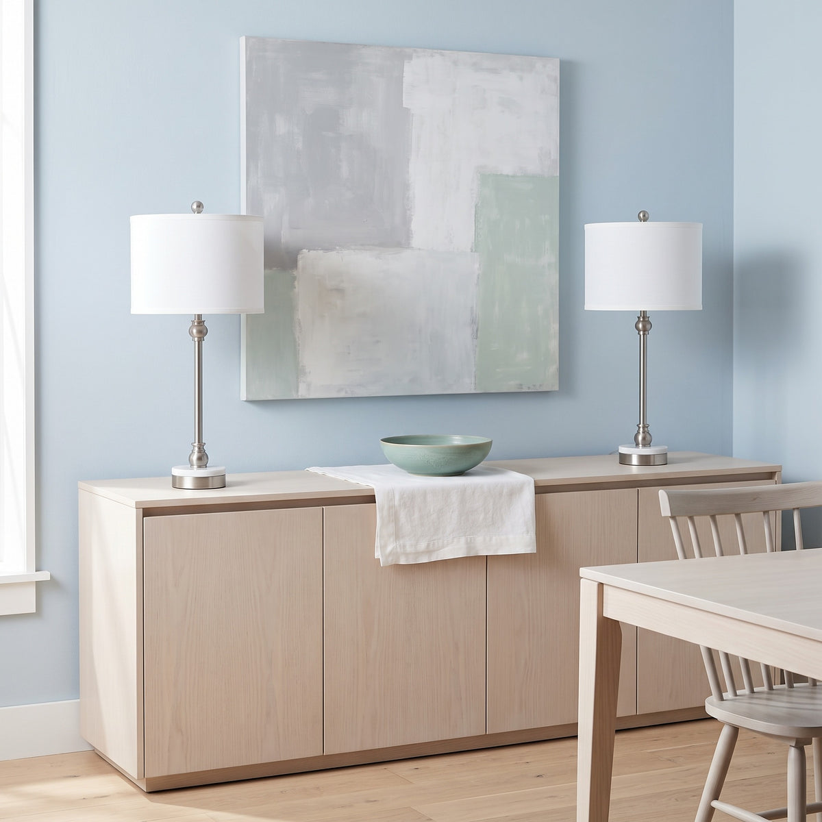 Pair of nickel table lamps with marble bases and white linen shades on a light wood sideboard