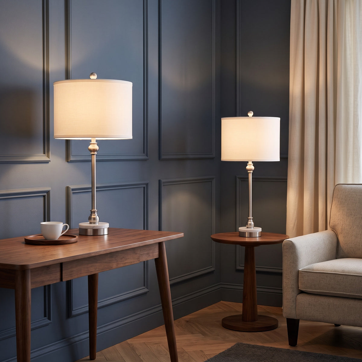Two nickel table lamps with white marble bases and linen drum shades, lit on walnut tables in a navy paneled room