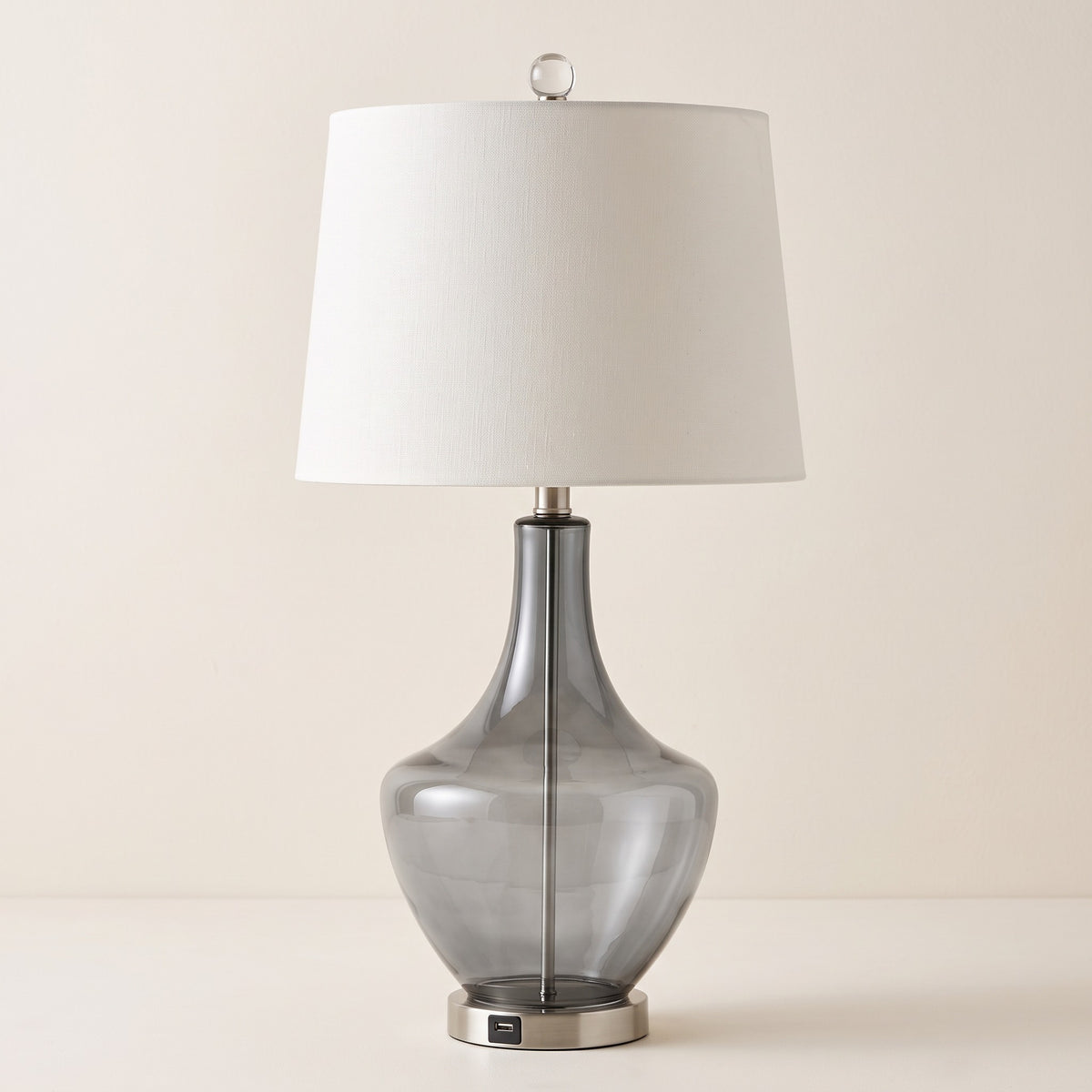 Smoky grey glass table lamp with white fabric shade and USB port base on an ivory backdrop