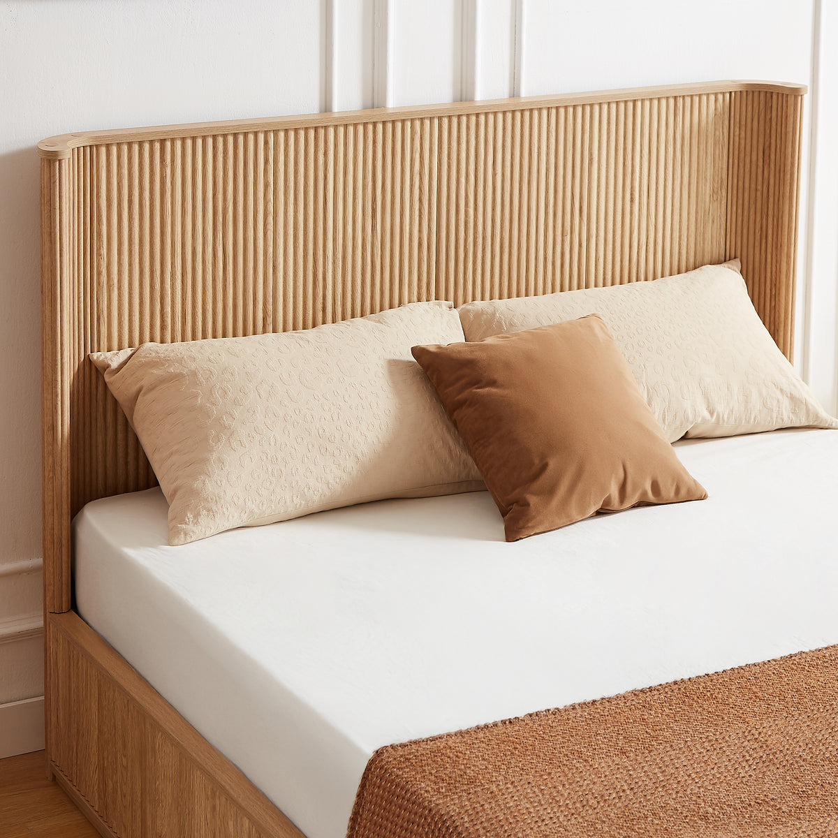 Close-up of the tall fluted natural oak headboard with beige and camel pillows