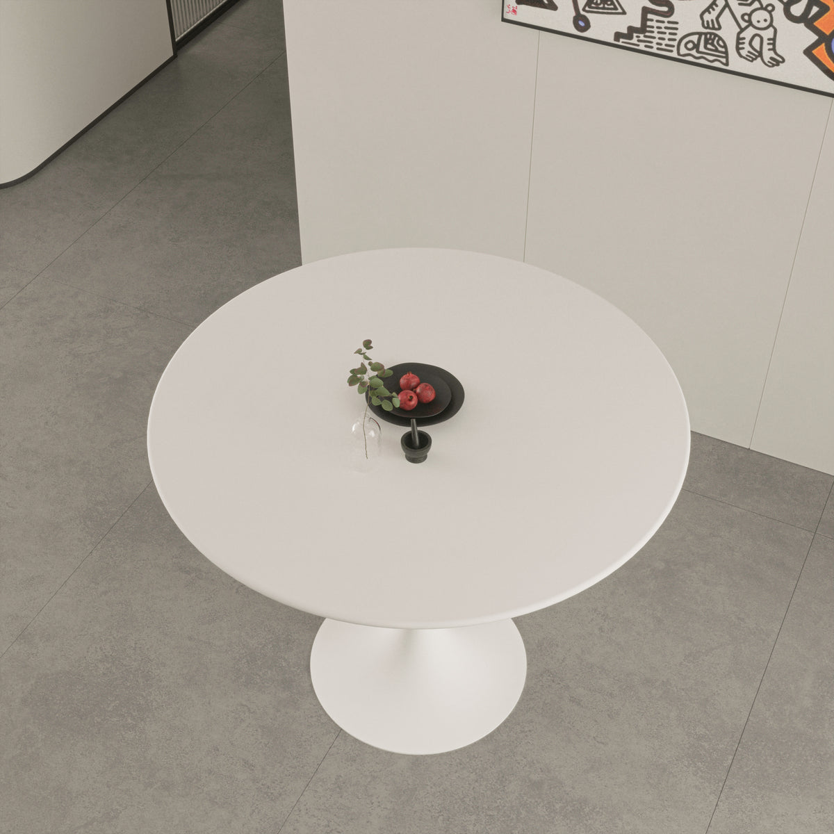 Overhead view of white round tulip dining table with a black plate of pomegranates on gray tile