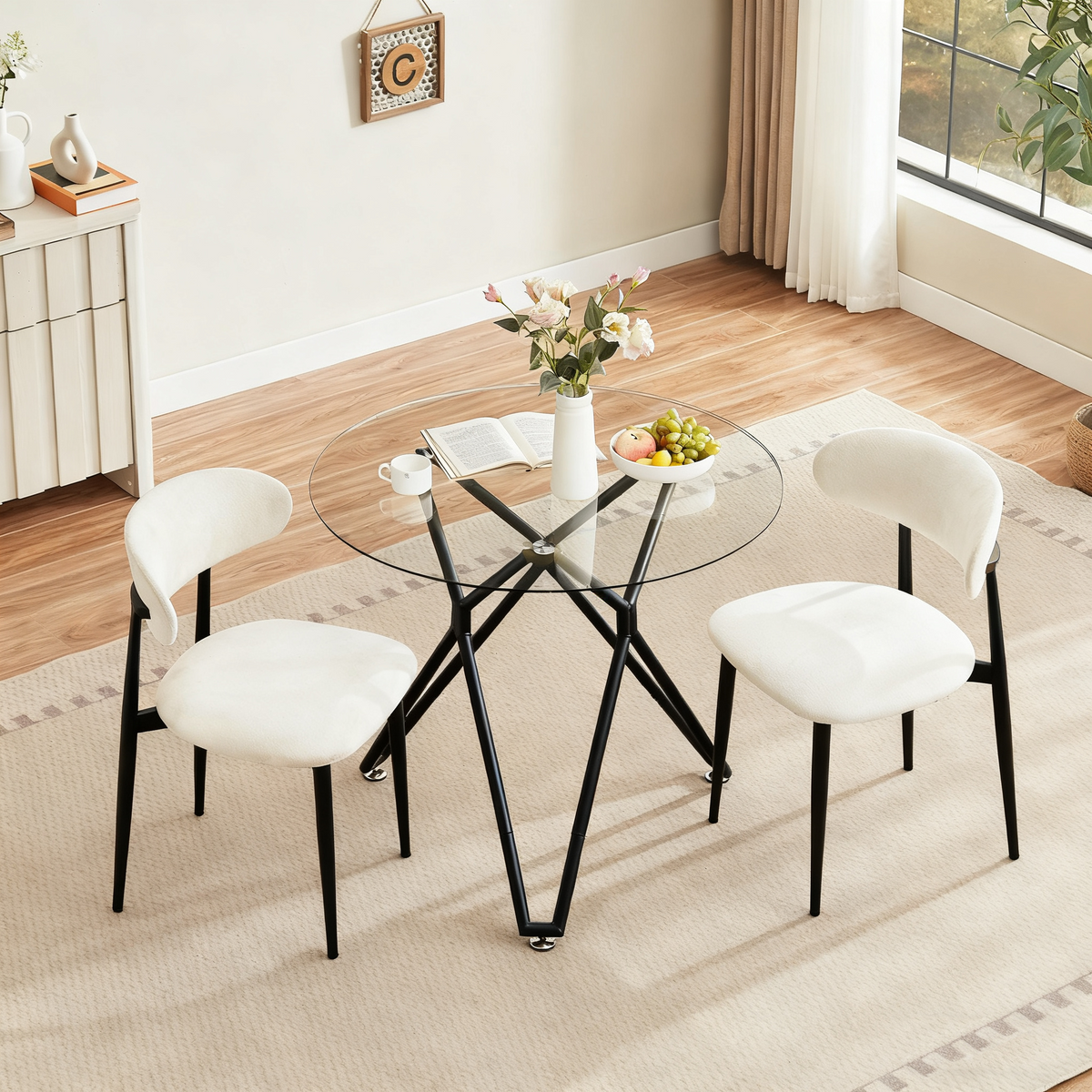 Overhead view of the round glass dining table with two cream boucle chairs, flowers and fruit in a dining nook